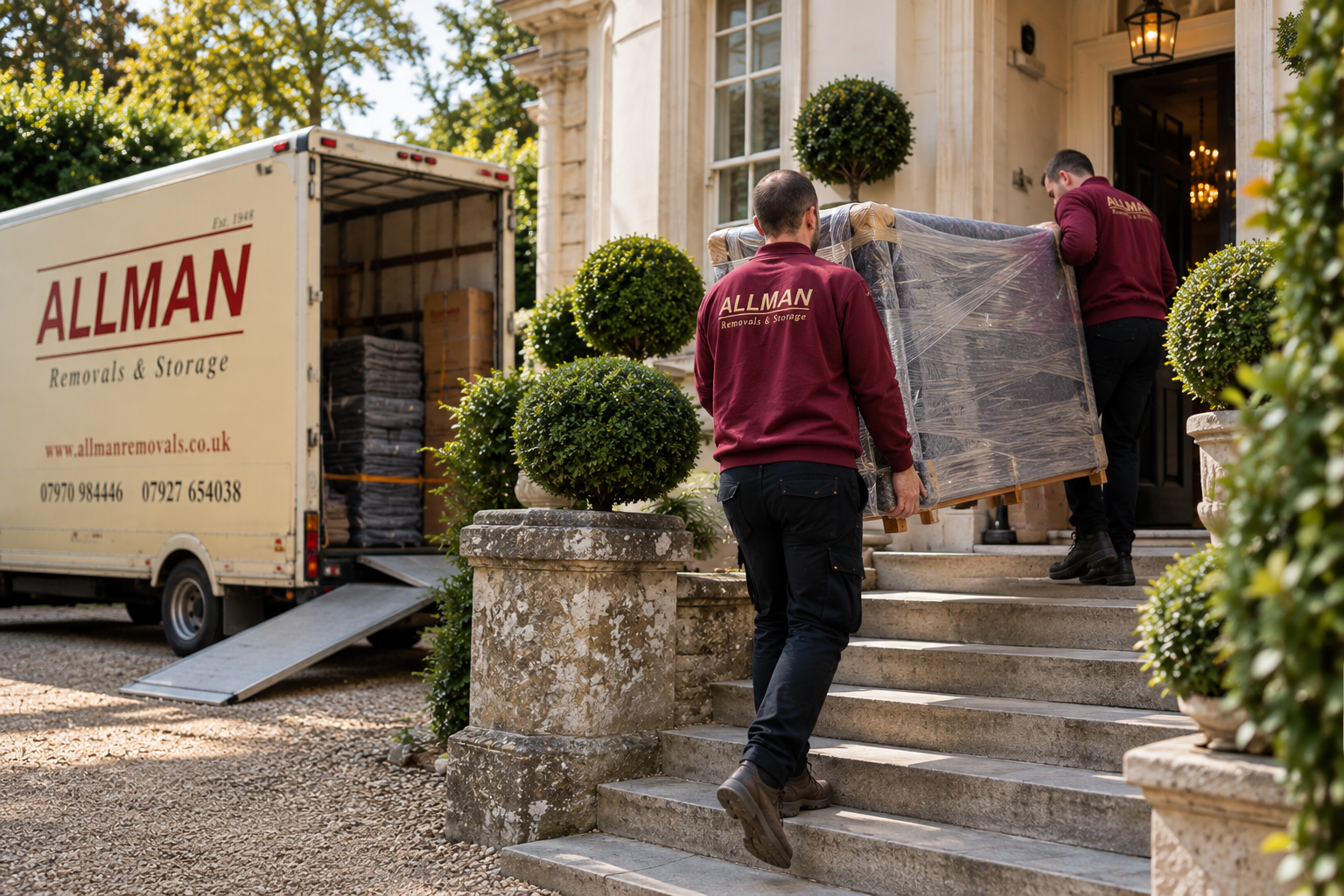 Two Allman team members carrying wrapped furniture up stone steps into a period home